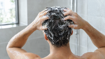 Close-up van achteren van nat donker haar met shampooschuim en vingertoppen die de hoofdhuid masseren, ketoconazol shampoo bij haaruitval